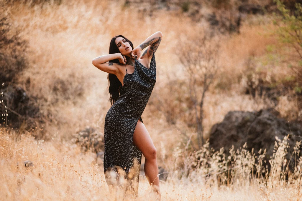 Woman in a black slip dress in golden grass at sunset