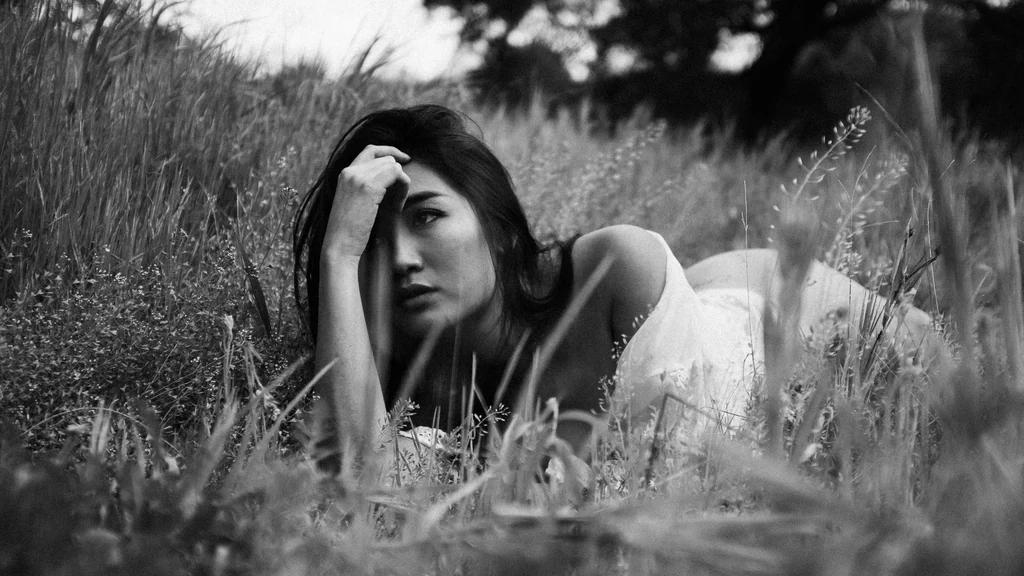 Woman in a white dress resting in tall grass, black and white
