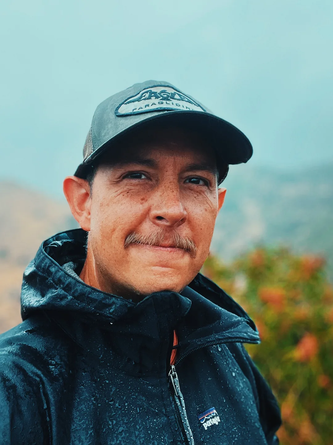 Kabir, the photographer, smiling in light rain on a mountain trail — warm candid portrait