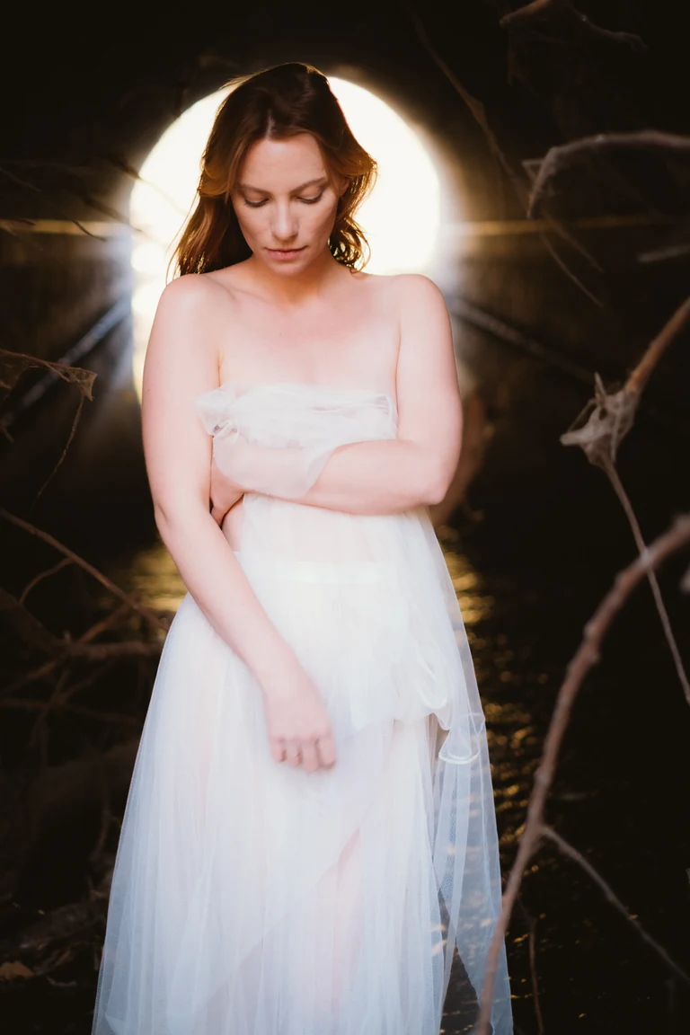 Fine art portrait — figure in white tulle in a circular woodland tunnel, backlit