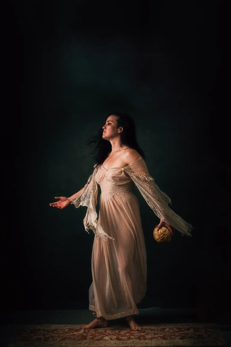 Woman in a flowing cream gown reaching outward, painterly studio light